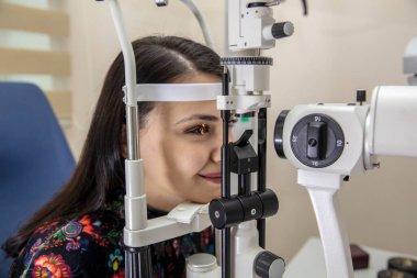 Göz bakımı için yüksek teknoloji konsepti. Göz doktorunun göz kliniğindeki göz doktoru, göz kontrolü için genç bir kadına dürbün lamba kullanıyor.. 