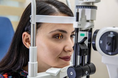 Göz bakımı için yüksek teknoloji konsepti. Göz doktorunun göz kliniğindeki göz doktoru, göz kontrolü için genç bir kadına dürbün lamba kullanıyor.. 