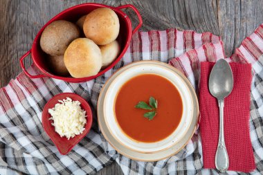 Peçete, kaşık, domates, maydanoz, tahta zemin üzerinde beyaz bir kasede domates çorbası..
