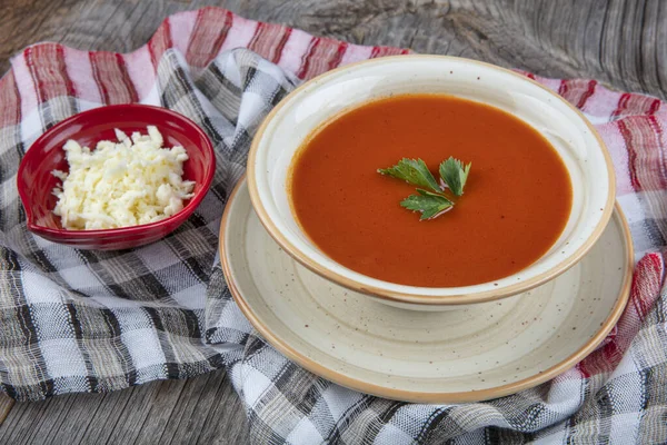 Peçete, kaşık, domates, maydanoz, tahta zemin üzerinde beyaz bir kasede domates çorbası..