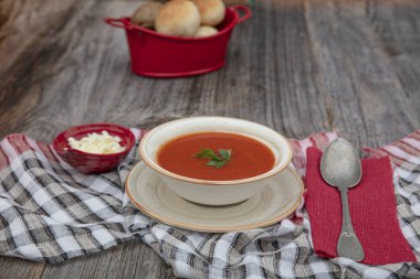 Peçete, kaşık, domates, maydanoz, tahta zemin üzerinde beyaz bir kasede domates çorbası..