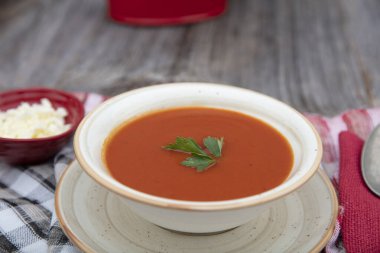 Peçete, kaşık, domates, maydanoz, tahta zemin üzerinde beyaz bir kasede domates çorbası..