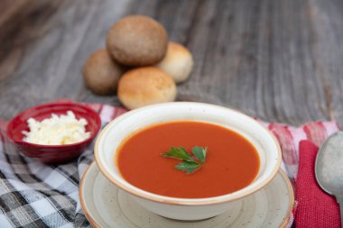 Peçete, kaşık, domates, maydanoz, tahta zemin üzerinde beyaz bir kasede domates çorbası..