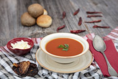 Peçete, kaşık, domates, maydanoz, tahta zemin üzerinde beyaz bir kasede domates çorbası..