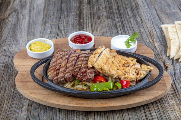 Combo Fajita; mexican steak and chicken fajitas in iron skillet with bell peppers and onion shot with warm colored light