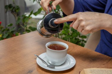 Kış çayı konsepti. Kadın elleri. Kız şeffaf cam çaydanlıktan limon ve portakallı narenciye çayını bardağa dolduruyor..