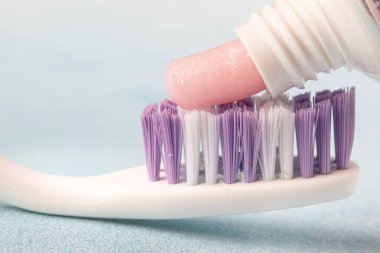 Diş fırçası ve pembe diş macunu mavi arka planda bir tüp diş macununun yanında. 