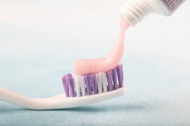 Diş fırçası ve pembe diş macunu mavi arka planda bir tüp diş macununun yanında. 