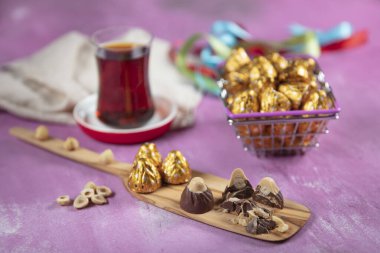 Hazelnut chocolate; Hazelnut Chocolate is wrapped in golden foil, on lila wooden background. Eid al-Fitr (Feast of Ramadan) concept. clipart