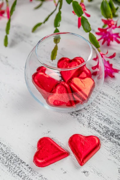 Heart shape chocolate candies wrapped in colorful foil for Valentine\'s Day. Valentine\'s Day background with chocolates hearts and red february blossoms.