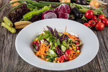 Taze sebzeli salata ve ahşap arka planda yeşiller.