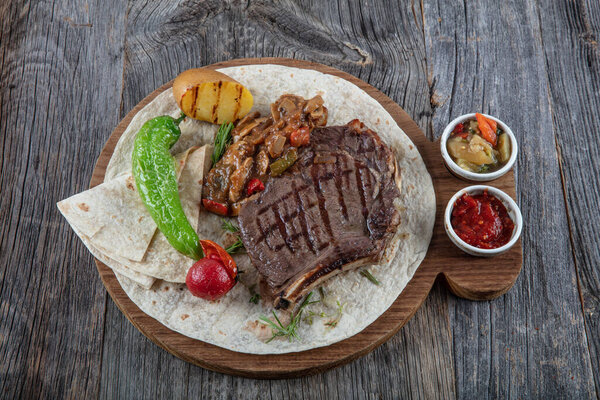 grilled beef steak with vegetables and spices on wooden board