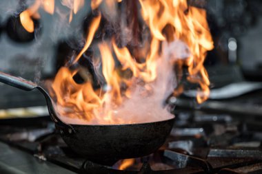 Kızartma Tavasında Ateşle Pişirilen Şef. Ticari bir mutfakta profesyonel bir aşçı alevli yemek pişirme stili. Aşçı, ticari mutfakta alevli tavada yemek pişiriyor..
