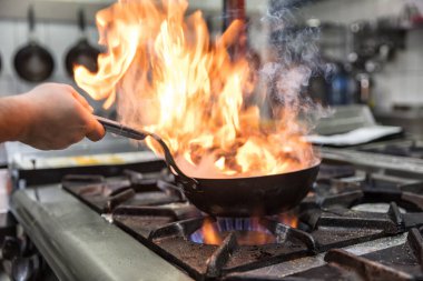 Kızartma Tavasında Ateşle Pişirilen Şef. Ticari bir mutfakta profesyonel bir aşçı alevli yemek pişirme stili. Aşçı, ticari mutfakta alevli tavada yemek pişiriyor..