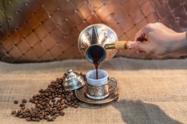 Kafe konsepti için fincandaki kahveyi dolduran kadın. Hasır arka planda bakır mutfak malzemesi..