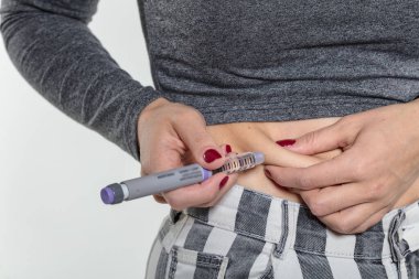 Diyabetli bir kadın hasta, evde bir kanepede iğneyle karın altı şırınga insülin iğnesi yapar.