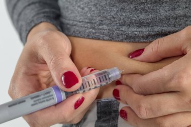 Diyabetli bir kadın hasta, evde bir kanepede iğneyle karın altı şırınga insülin iğnesi yapar.