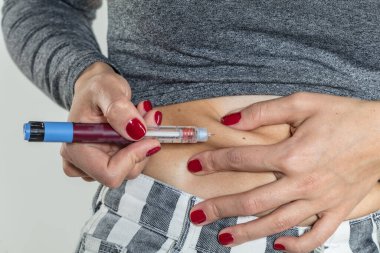 Diyabetli bir kadın hasta, evde bir kanepede iğneyle karın altı şırınga insülin iğnesi yapar.