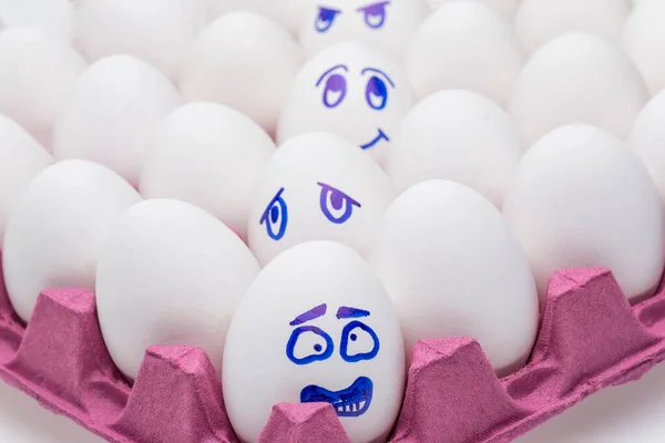 Funny eggs. One happy smiling egg amongst sad, angry and envious crowd of eggs isolated on white background