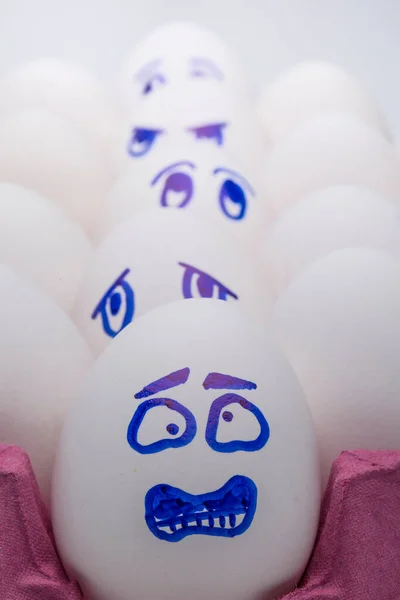 Funny eggs. One happy smiling egg amongst sad, angry and envious crowd of eggs isolated on white background
