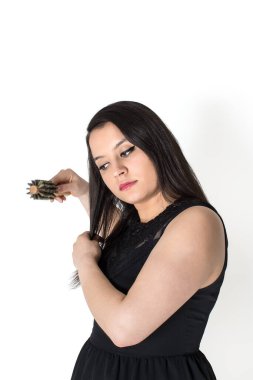 beautiful brunette young woman with long hair in a black dress brushing her hair isolated on white background