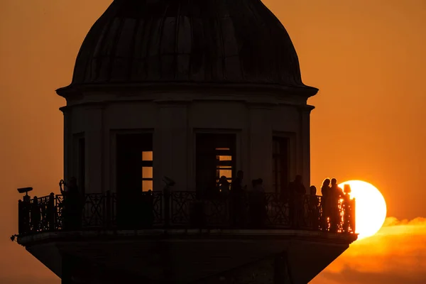 silhouette of people on the lighthouse with sunset in the background.