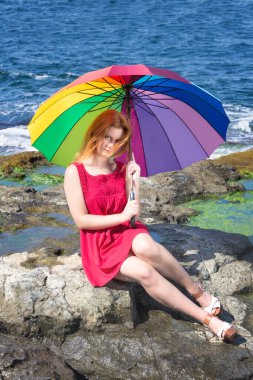 Kayalık sahilde renkli şemsiyeli genç ve güzel bir kadın.
