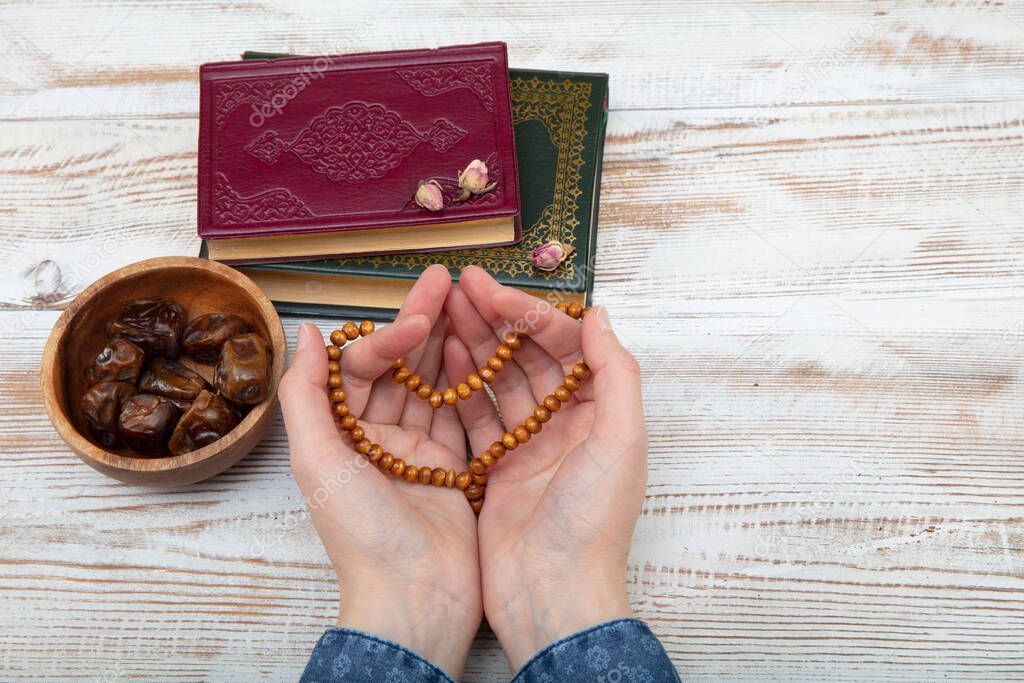 Koran - holy book of Muslims with rosary , date and dried flowers. ramadan concept. Praying woman.