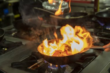 Kızartma Tavasında Ateşle Pişirilen Şef. Ticari bir mutfakta profesyonel bir aşçı alevli yemek pişirme stili. Aşçı, ticari mutfakta alevli tavada yemek pişiriyor..