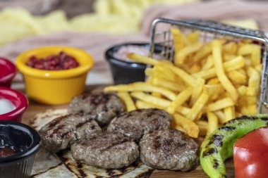 Türk köftesi, (Türk yemeği Kofte veya Kofta) kırmızı biber, domates, patates kızartması ve ahşap kesim tahtasının üzerinde soğan.