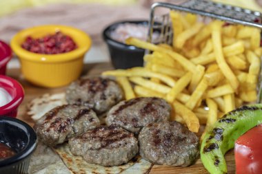 Türk köftesi, (Türk yemeği Kofte veya Kofta) kırmızı biber, domates, patates kızartması ve ahşap kesim tahtasının üzerinde soğan.