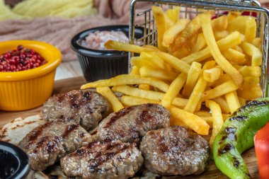 Türk köftesi, (Türk yemeği Kofte veya Kofta) kırmızı biber, domates, patates kızartması ve ahşap kesim tahtasının üzerinde soğan.