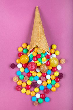 Renkli şekerli dondurma külahları, tatlı jölesi, çubukta lolipop, pembe arka planda çok renkli şekerlerin serpilmesi. Üst Manzara 'da dümdüz yatıyordu. Boşluğu kopyala.