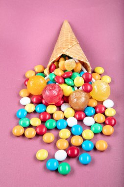 Renkli şekerli dondurma külahları, tatlı jölesi, çubukta lolipop, pembe arka planda çok renkli şekerlerin serpilmesi. Üst Manzara 'da dümdüz yatıyordu. Boşluğu kopyala.