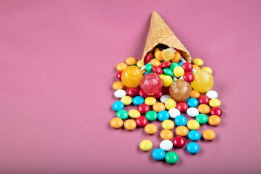 Renkli şekerli dondurma külahları, tatlı jölesi, çubukta lolipop, pembe arka planda çok renkli şekerlerin serpilmesi. Üst Manzara 'da dümdüz yatıyordu. Boşluğu kopyala.