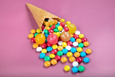 Renkli şekerli dondurma külahları, tatlı jölesi, çubukta lolipop, pembe arka planda çok renkli şekerlerin serpilmesi. Üst Manzara 'da dümdüz yatıyordu. Boşluğu kopyala.