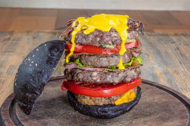 Erimiş peynirli büyük bir çizburger. Lezzetli iştah açıcı, sağlıklı vejetaryen siyah burgerler ahşap masada. Kopya uzayı ile yatay. Sağlıklı yemek kavramı, temiz yemek..