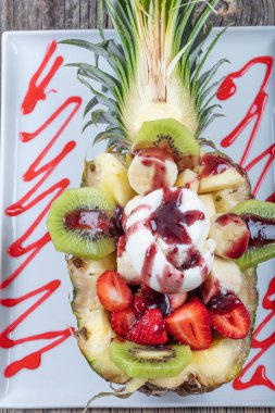 Çilekli, muzlu ve kivili bir top dondurmayla ananas ikiye bölünmüş. Tatlı diyeti için mükemmel ya da sağlıklı bir yemek için. Sağlıklı çiğ yiyecekler için aşk.