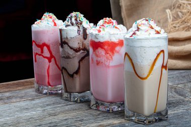 Dört bardak renkli milkshake kokteyli - Çikolatalı milkshake, çilekli milkshake, karamelli milkshake, ahşap zeminde taze böğürtlenlerle süslenmiş milkshake.