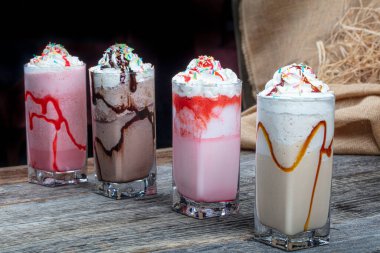 Dört bardak renkli milkshake kokteyli - Çikolatalı milkshake, çilekli milkshake, karamelli milkshake, ahşap zeminde taze böğürtlenlerle süslenmiş milkshake.