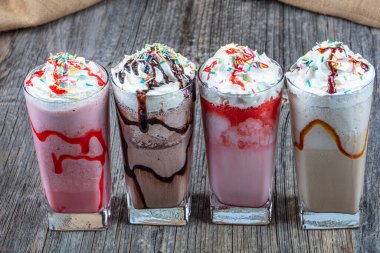 Dört bardak renkli milkshake kokteyli - Çikolatalı milkshake, çilekli milkshake, karamelli milkshake, ahşap zeminde taze böğürtlenlerle süslenmiş milkshake.