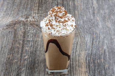 Soğuk kahve içen frappe (frappuccino), krema ve karamel şurubuyla, pipet ve kahve taneleriyle ahşap bir masanın üzerinde, boşluğu kopyala.