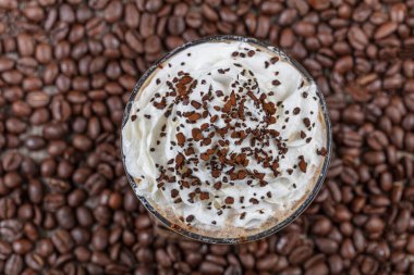 Soğuk kahve içen frappe (frappuccino), krema ve karamel şurubuyla, pipet ve kahve taneleriyle ahşap bir masanın üzerinde, boşluğu kopyala.