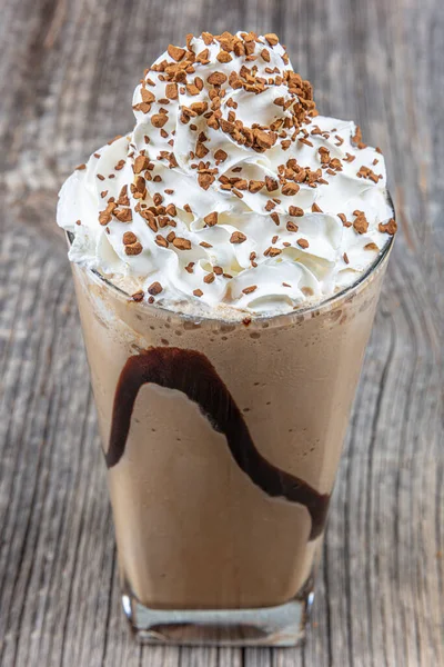 Cold coffee drink frappe (frappuccino), with whipped cream and caramel syrup, with straws and grains of coffee on a wooden table, copy space.