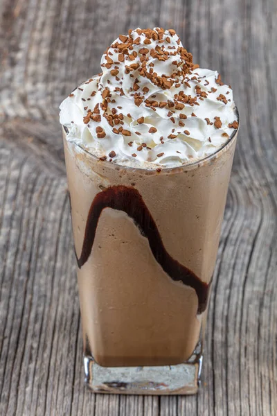 Cold coffee drink frappe (frappuccino), with whipped cream and caramel syrup, with straws and grains of coffee on a wooden table, copy space.