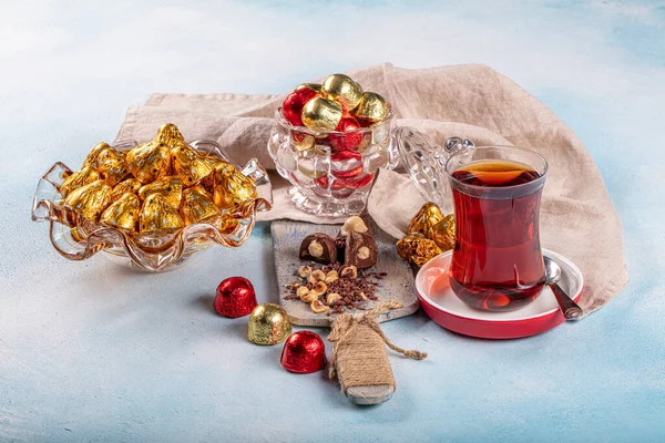 Chocolate candy in shiny wrapper. Delicious chocolate candies and tea on wooden background. Ramadan Eid (Ramadan feast) Concept.