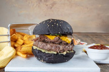 Siyah çörekli sığır burger, marul, mayonez ve ketçap ile birlikte koyu bir arka planda, sayaç üzerinde kahverengi kağıt parçaları üzerinde servis edilir..