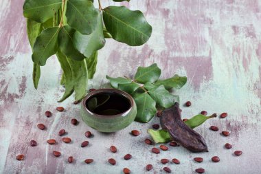 Karob fasulyesi (Harnup). Tahta arka planda yaprakları ve tohumları olan sağlıklı organik keçiboynuzu tohumları..