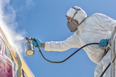 Uçak boyama ve kum püskürtme. Sprey boya, uçak kanadı. Hava fırçası kullanan örtülü bir işçi.