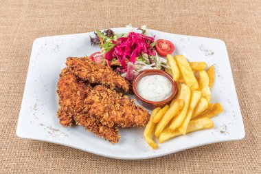 Lezzetli kızarmış tavuk göğsü şeritlerini beyaz tabakta, domates soslu ve limon dilimli eski ahşap masa üzerinde, açık hava pikniği ya da parti için kolay tarif, yukarıdan görüş.